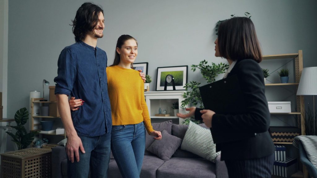 Ein junges Paar trifft sich in einem stilvollen Interieur mit einem Immobilienmakler und bespricht verschiedene Hausoptionen.