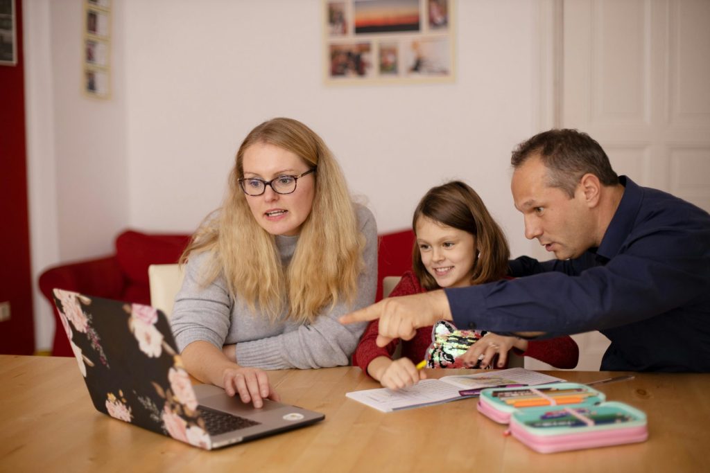 Eine Familie lernt gemeinsam zu Hause mit einem Laptop, wobei Zusammenarbeit und Bildung im Vordergrund stehen.